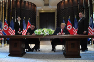 Prezydent Donald Trump i przywódca Korei Płn. Kim Dzong Un podpisują dokumenty, podczas gdy sekretarz stanu Mike Pompeo (po prawej) oraz Kim Jo Dzong, siostra Kima (po lewej), przyglądają się ceremonii w trakcie historycznego szczytu USA – Korea Płn., w hotelu Capella, na wyspie Sentosa, Singapur, 12.06.2018 r. (SAUL LOEB/AFP/Getty Images)