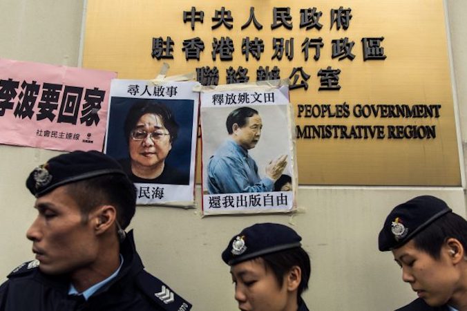 Policjanci przechodzą obok plakatów z portretami zaginionych osób: (od lewej) Gui Minhaia, jednego z pięciu zaginionych wydawców z Mighty Current, oraz Yao Wentiana, wydawcy z Hongkongu, który został wtrącony do więzienia na 10 lat za przygotowanie do wydania książki nastawionej krytycznie do chińskiego przywództwa. Zdjęcia przyklejone do tablicy z nazwą chińskiego biura łącznikowego w Hongkongu, 3.01.2016 r. (ANTHONY WALLACE/AFP/Getty Images)