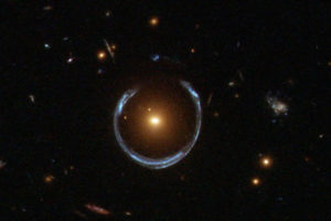 Galaktyka LRG 3-757 zniekształca obraz dalszej galaktyki. Przykład soczewkowania grawitacyjnego, którego mniej spektakularną formą jest mikrosoczewkowanie grawitacyjne (<a href="https://commons.wikimedia.org/w/index.php?curid=17750428">Lensshoe_hubble.jpg</a>: ESA/Hubble &amp; NASAderivative work: Bulwersator, talk – <a href="https://commons.wikimedia.org/w/index.php?curid=17750428">Lensshoe_hubble.jpg</a> / <a href="https://commons.wikimedia.org/w/index.php?curid=17750437">domena publiczna</a>)