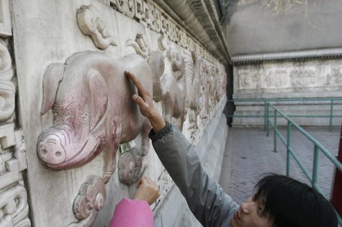 Mężczyzna dotyka płaskorzeźby świni – jednej z dwunastu płaskorzeźb przedstawiających zwierzęta z chińskiego kalendarza księżycowego – w Świątyni Białej Chmury w Pekinie, 15.02.2007 r. Rok Świni, naznaczony niepokojącymi wiadomościami gospodarczymi dla Chin, rozpoczął się 5 lutego 2019 r. (FREDERIC J. BROWN/AFP/Getty Images)