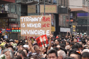Jeden z protestujących trzyma transparent „Tyrania nigdy nie jest niezwyciężona” w nawiązaniu do władz Hongkongu pod przewodnictwem Carrie Lam, 16.06.2019 r. Kolejny protestujący trzyma czerwoną tablicę z chińskim napisem „Dzieci to nie uczestnicy zamieszek” (Yu Gang / The Epoch Times)