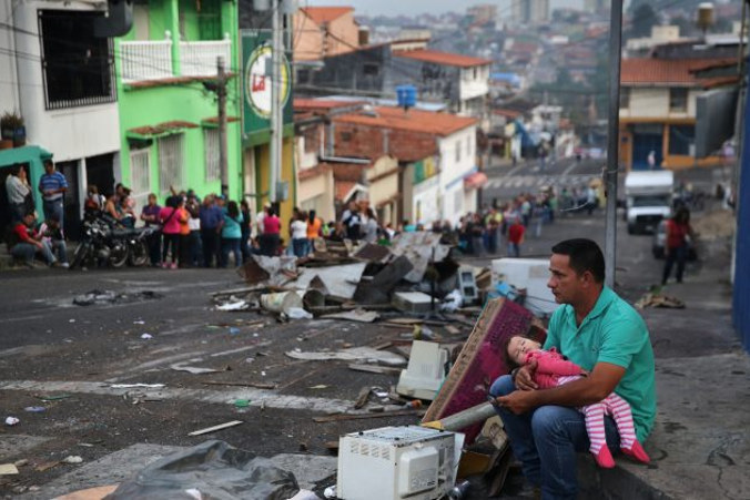 Ojciec i córka odpoczywają, podczas gdy ktoś trzyma dla nich miejsce w długiej kolejce, w której przed wschodem słońca ludzie stoją, aby kupić podstawowe produkty żywnościowe w supermarkecie, San Cristóbal, stolica stanu Táchira, Wenezuela, 8.03.2014 r. (John Moore / Getty Images)