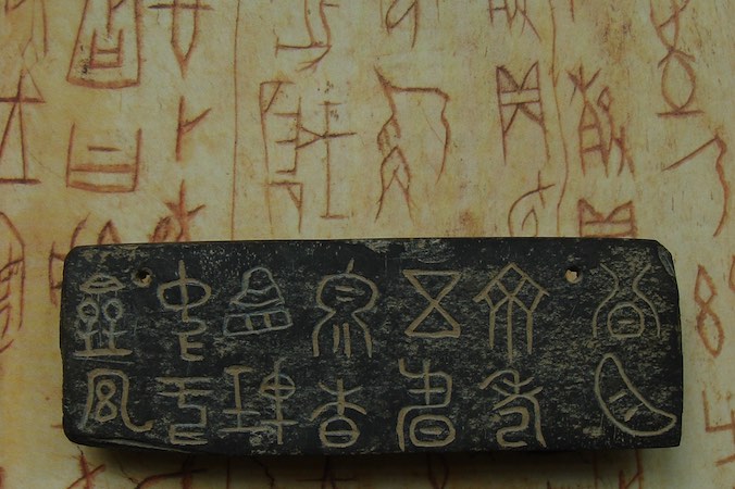 Inskrypcje w kamieniu z Zachodniej Dynastii Zhou na tle inskrypcji wróżebnych z okresu dynastii Shang (Liuzpy – praca własna, zdjęcie modyfikowane, <a href="https://creativecommons.org/licenses/by-sa/3.0/">CC BY-SA 3.0</a> / <a href="https://commons.wikimedia.org/w/index.php?curid=25487409">Wikimedia</a>)