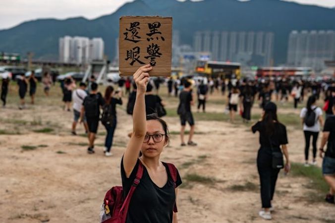 Protestująca trzyma tabliczkę z hasłem, które można przetłumaczyć jako „policjancie, zapłacisz za oko”, na zewnątrz międzynarodowego lotniska w Hongkongu, gdy protestujący wycofują się podczas demonstracji, Hongkong, 12.08.2019 r. (Anthony Kwan / Getty Images)