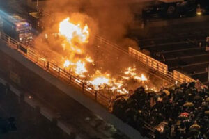 Samochód policyjny stoi w ogniu, podczas gdy protestujący i policja ścierają się na moście na Uniwersytecie Politechnicznym w Hongkongu, 17.11.2019 r. (Anthony Kwan / Getty Images)