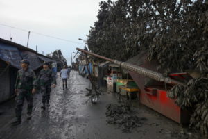Policjanci przechodzą obok uszkodzonego słupa, po tym jak wulkan Taal wyrzucił chmurę popiołów na wysokość 1 km, Talisay w prowincji Batangas, Filipiny, 13.01.2020 r.<br/>(MARK R. CRISTINO/PAP/EPA)