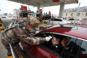 Funkcjonariusz milicji sprawdza temperaturę ciała kierowcy w pojeździe przy bramce na płatnej autostradzie w Wuhan, prowincja Hubei w środkowych Chinach, 23.01.2020 r.<br/>(YUAN ZHENG/PAP/EPA)