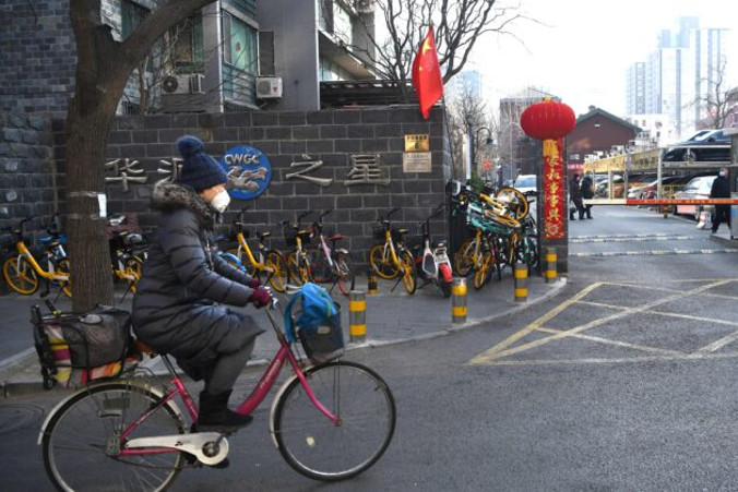 Rowerzystka w masce na twarzy mija rowery ułożone jako barykada, aby zatarasować boczne wejście do osiedla, co zmusza odwiedzających do zarejestrowania się u strażników przy głównym wejściu, Pekin, 30.01.2020 r.<br/>(NOEL CELIS/AFP via Getty Images)