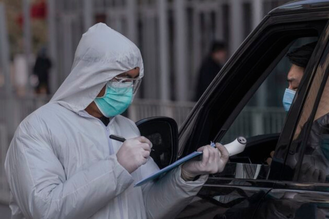 Pracownik w stroju ochronnym zapisuje nazwisko kierowcy podjeżdżającego samochodem do budynku biurowego, Pekin, 10.02.2020 r. (Kevin Frayer/Getty Images)