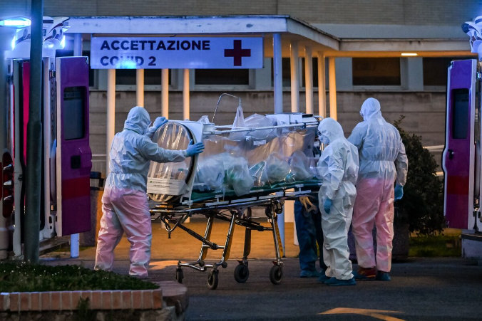 Pracownicy medyczni w kombinezonach zabierają pacjenta w stanie wymagającym intensywnej terapii do nowo wybudowanego szpitala tymczasowego Columbus Covid 2 w szpitalu Gemelli w Rzymie, 16.03.2020 r.<br /> (Andreas Solaro/AFP via Getty Images)
