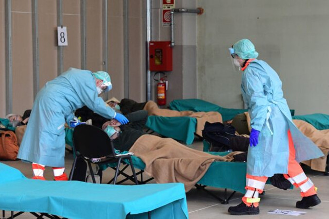 Pracownicy szpitala w maskach i odzieży ochronnej opiekują się pacjentem w tymczasowym obiekcie postawionym przed oddziałem ratunkowym szpitala w miejscowości Brescia, Lombardia we Włoszech, 13.03.2020 r.<br/>(Miguel Medina/AFP via Getty Images)