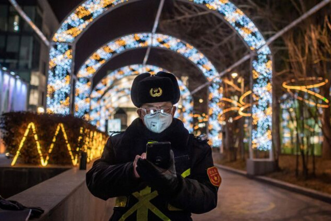 Ochroniarz sprawdza telefon komórkowy, pilnując wejścia do prawie pustego centrum handlowego w Pekinie, 27.02.2020 r. (NICOLAS ASFOURI/AFP via Getty Images)