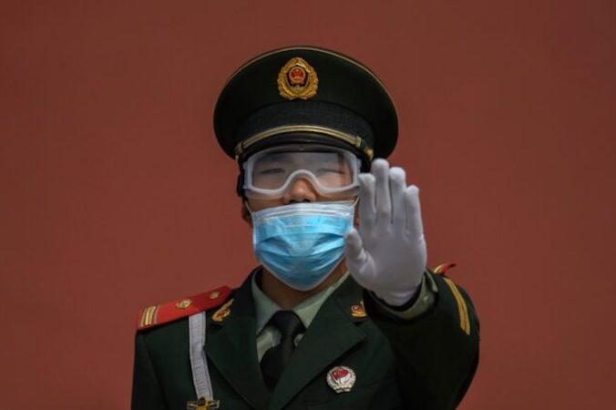 Funkcjonariusz chińskiej policji paramilitarnej z założoną na twarzy maską ochronną gestykuluje, trzymając wartę przy wejściu do Zakazanego Miasta, które zostało ponownie otwarte dla ograniczonej liczby zwiedzających, Pekin, Chiny, 1.05.2020 r. (Kevin Frayer / Getty Images)