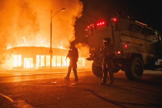 Policyjny pojazd opancerzony patroluje skrzyżowanie przy płonącym budynku podpalonym przez uczestników zamieszek w mieście Kenosha w stanie Wisconsin, 24.08.2020 r. (Brandon Bell / Getty Images)
