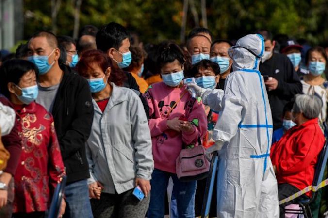 Pracownik służby zdrowia sprawdza temperaturę mieszkańców, którzy ustawiają się w kolejce do badania na obecność COVID-19 w Qingdao, w prowincji Shandong we wschodnich Chinach, 12.10.2020 r. (STR/AFP/Getty Images)