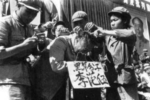 Podczas rewolucji kulturowej w 1966 roku towarzysze partii komunistycznej wieszają karton z napisem na szyi Chińczyka. Na kartonie napisane jest nazwisko mężczyzny i szykany, że należy do „czarnej klasy” (domena publiczna)