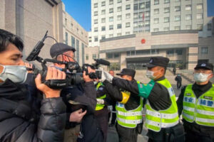 Policja próbuje powstrzymać dziennikarzy przed nagrywaniem materiału filmowego przed Sądem Ludowym Nowej Dzielnicy Pudong w Szanghaju, w którym wydano wyrok w sprawie dziennikarki obywatelskiej Zhang Zhan, Szanghaj, Chiny, 28.12.2020 r. (Leo Ramirez/AFP via Getty Images)