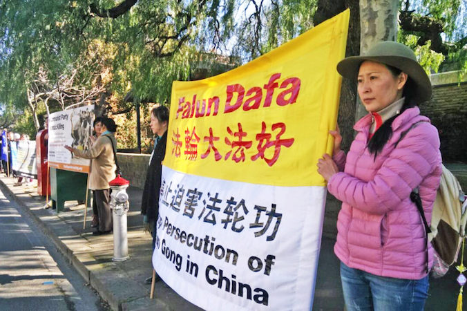 Angel trzyma baner „Stop prześladowaniom Falun Gong” naprzeciw głównego wejścia do chińskiego konsulatu w Toorak, Melbourne, Australia (dzięki uprzejmości Angel)