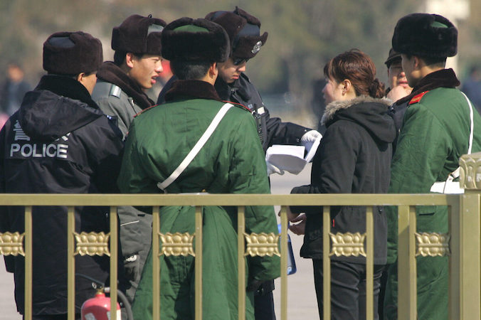 Policjanci i funkcjonariusze oddziałów paramilitarnych otoczyli kobietę, a policjant czyta jej petycję. Dzieje się to podczas zwiększonych środków bezpieczeństwa na placu Tiananmen w Pekinie, 6.03.2007 r. (FREDERIC J. BROWN/AFP via Getty Images)