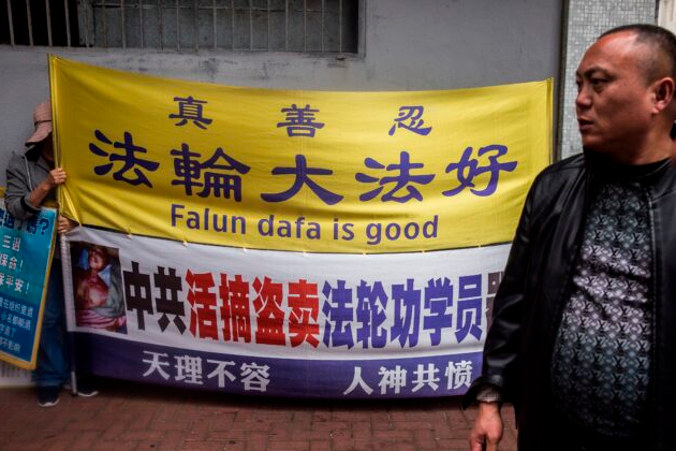 Praktykujący Falun Gong (po lewej) trzyma transparent obok mężczyzny (po prawej) z grupy wycieczkowej z Chin kontynentalnych, region Koulun w Hongkongu, 6.01.2019 r. (Isaac Lawrence/AFP via Getty Images)