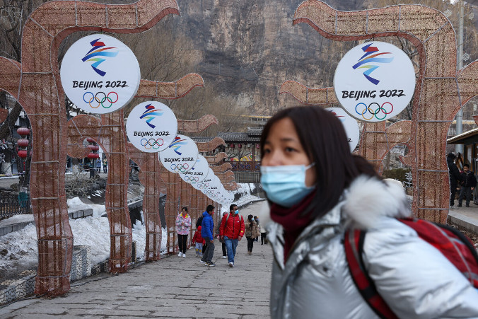 Przechodnie noszą maski ochronne podczas Yanqing Ice Festival w Pekinie, w tle widoczne logo Zimowych Igrzysk Olimpijskich w Pekinie zaplanowanych na 2022 r., 26.02.2021 r. (Lintao Zhang / Getty Images)