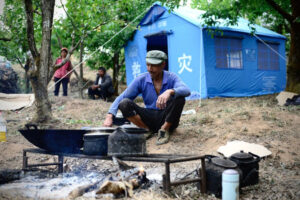 Mężczyzna gotuje posiłek przed namiotami ustawionymi dla osób wysiedlonych na skutek nocnego trzęsienia ziemi w powiecie Yangbi, prefektura Dali w południowo-zachodniej prowincji Yunnan, Chiny, 22.05.2021 r. (AFP via Getty Images)