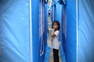 Dziewczynka wygląda spomiędzy namiotów ustawionych dla osób wysiedlonych na skutek nocnego trzęsienia ziemi w powiecie Yangbi, prefektura Dali w południowo-zachodniej prowincji Yunnan, Chiny, 22.05.2021 r. (AFP via Getty Images)