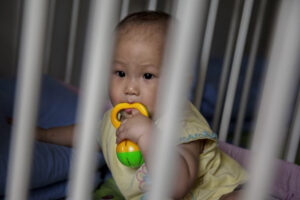 Mała osierocona dziewczynka siedzi w łóżeczku w ośrodku opieki zastępczej w Pekinie, 2.04.2014 r. (Kevin Frayer / Getty Images)