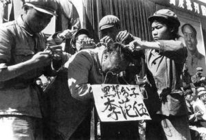 Podczas rewolucji kulturowej towarzysze z partii komunistycznej wieszają na szyi mężczyzny tekturową tabliczkę. Na niej wypisane jest jego nazwisko oraz to, że jest oskarżony o przynależność do „czarnej klasy”, 1966 r. (domena publiczna)