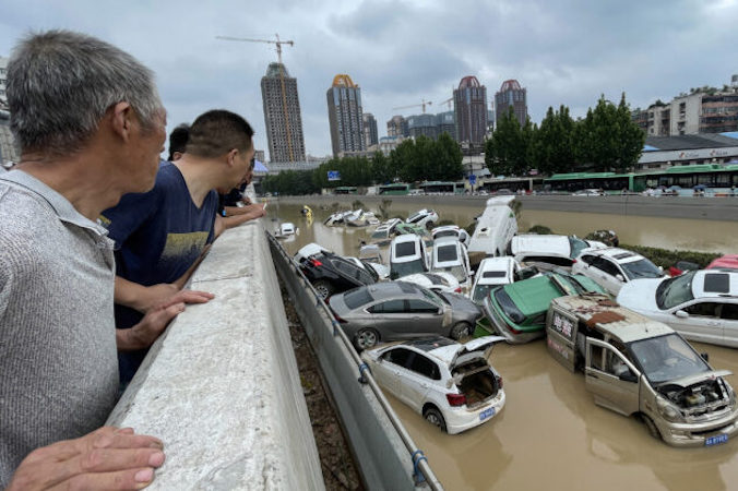 Ludzie patrzą na samochody stojące w wodzie po ulewnych deszczach w mieście Zhengzhou, prowincja Henan, Chiny, 21.07.2021 r. (STR/AFP via Getty Images)