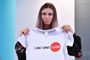 Białoruska biegaczka Kryscina Cimanouska podczas konferencji prasowej prezentuje koszulkę z napisem: I just want to run, Warszawa, 5.08.2021 r. (Radek Pietruszka / PAP)