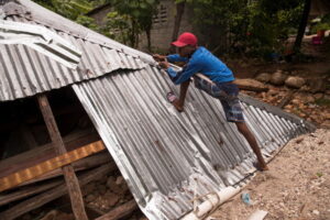 Mężczyzna w deszczu wykorzystuje materiały ze zniszczonego domu podczas burzy tropikalnej Grace, Camp-Perrin na Haiti, 17.08.2021 r. (Orlando Barria/PAP/EPA)