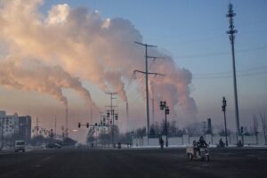 Chińscy robotnicy dojeżdżają do pracy, a w oddali z elektrowni węglowej w Shanxi unosi się dym, Chiny, 25.11.2015 r. (Kevin Frayer / Getty Images)