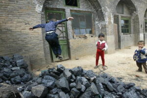 Dzieci bawią się obok sterty węgla przed domami zbudowanymi w jaskiniach, Xiaoyi, na wzgórzach niedaleko Taiyuan, prowincja Shanxi na północy Chin, w której wydobywa się najwięcej węgla w kraju, 26.05.2004 r. (FREDERIC J. BROWN/AFP via Getty Images)