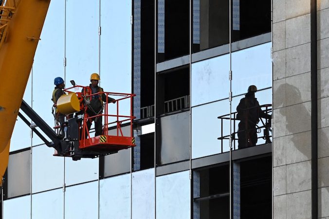Robotnicy przygotowują się do montażu paneli okiennych na placu budowy w Pekinie, 19.10.2021 r. (Greg Baker/AFP via Getty Images)