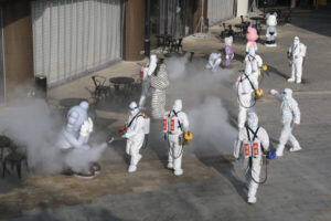 Pracownicy ubrani w środki ochrony osobistej rozpylają środki dezynfekujące na zewnątrz centrum handlowego w Xi’an, Chiny, 11.01.2022 r. (STR/AFP via Getty Images)