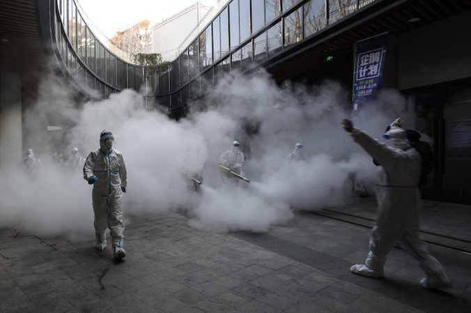 Pracownicy ubrani w sprzęt ochrony osobistej (PPE) rozpylają środki dezynfekujące przed centrum handlowym w Xi’an, Chiny, 11.01.2022 r. (STR/AFP via Getty Images)