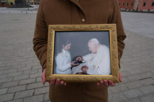 Maria trzyma w rękach zdjęcie z Watykanu, z audiencji u papieża Jana Pawła II, która miała miejsce 14.05.2002 r., pl. Zamkowy w Warszawie, 19.04.2022 r. (The Epoch Times)