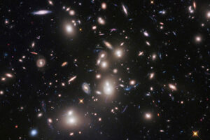 Zdjęcie ilustracyjne. Ta ogromna gromada galaktyk, nazwana Abell 2744 i nosząca przydomek Gromada Pandory, została sfotografowana przez Kosmiczny Teleskop Hubble’a w ramach programu Pola Graniczne, w którym Hubble wraz z innymi wielkimi obserwatoriami NASA bada wczesny Wszechświat, przepatrując duże gromady galaktyk. Gromada jest tak masywna, że jej potężna grawitacja ugina światło galaktyk znajdujących się daleko za nią, sprawiając, że obiekty tła wydają się większe i jaśniejsze, co jest zjawiskiem zwanym soczewkowaniem grawitacyjnym. Soczewkowanie grawitacyjne pozwala teleskopom zobaczyć bardzo odległe galaktyki, które w innym przypadku byłyby poza ich zasięgiem (<a href="https://www.flickr.com/photos/144614754@N02/32830077718/">NASA Hubble</a>, <a href="https://creativecommons.org/licenses/by/2.0/">CC BY 2.0</a>, zdjęcie modyfikowane / <a href="https://commons.wikimedia.org/w/index.php?curid=87486759">Wikimedia</a>)