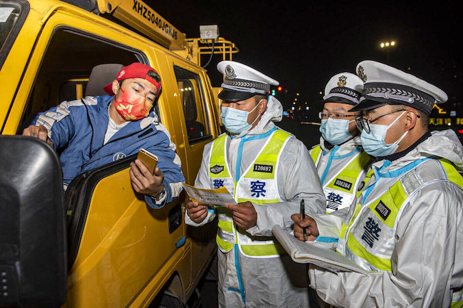 Policjanci sprawdzają dokumentację kierowcy ciężarówki (z lewej) w punkcie kontrolnym w Ningbo, prowincja Zhejiang, Chiny, 18.12.2021 r. (STR/AFP via Getty Images)