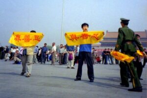 Chiński policjant zbliża się do praktykującego Falun Gong na placu Tiananmen w Pekinie, gdy ten trzyma transparent z chińskimi znakami „Prawda, Życzliwość i Cierpliwość”, które są głównymi zasadami Falun Gong (dzięki uprzejmości Minghui.org)