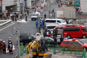 Policja i strażacy gromadzą się wokół stacji Yamato-Saidaiji kolei Kintetsu w Narze, Japonia, w miejscu, gdzie były premier Shinzō Abe został postrzelony, 8.07.2022 r. przez zamachowca (JIJI PRESS/PAP/EPA)