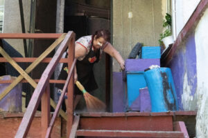 Kobieta sprząta ganek w zachowanej części budynku podczas akcji ratunkowej ukraińskich służb na gruzach budynku mieszkalnego w Charkowie trafionego przez rosyjską rakietę, 9.07.2022 r. (Mykola Kalyeniak / PAP)