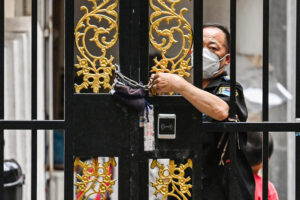  Pracownik ochrony zamyka drzwi łańcuchem w dzielnicy objętej blokadą COVID-19 w dzielnicy Jing’an w Szanghaju, 2.06.2022 r. (Hector Retamal/AFP via Getty Images)