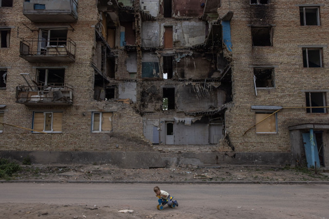 Chlopiec bawi się przed zniszczonym budynkiem mieszkalnym w Horence, obwód kijowski, Ukraina, 17.06.2022 r., wydane 23.08.2022 r. (ROMAN PILIPEY/PAP/EPA)