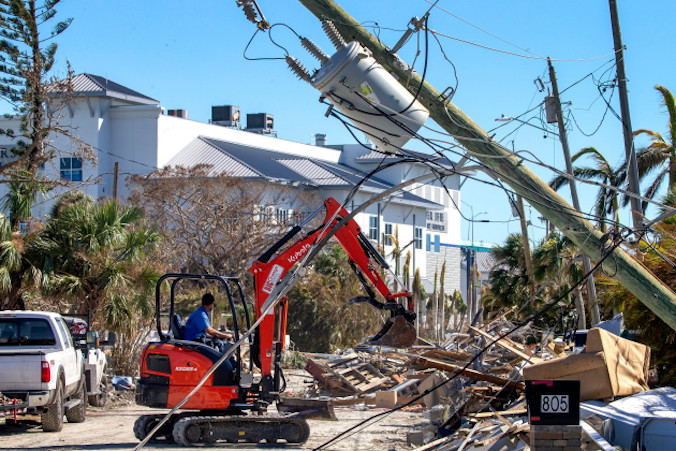 Koparka podnosi gruz przed powalonym słupem energetycznym na wyspie San Carlos po przejściu huraganu Ian w Fort Myers Beach, Floryda, USA, 2.10.2022 r. (CRISTOBAL HERRERA-ULASHKEVICH/PAP/EPA)
