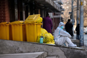 Pracownik ubrany w środki ochrony osobistej (PPE) siedzi obok odpadów przed kliniką leczenia gorączki podczas pandemii COVID-19, Pekin, 19.12.2022 r. (Noel Celis/AFP via Getty Images)