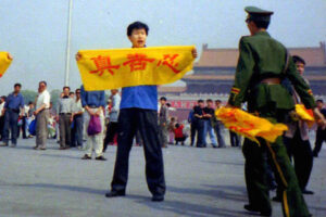 Chiński policjant na placu Tiananmen w Pekinie zbliża się do praktykującego Falun Gong, który trzyma transparent z chińskimi znakami oznaczającymi „prawdę, życzliwość i cierpliwość”, podstawowe zasady Falun Gong (dzięki uprzejmości Minghui.org)