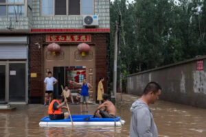 Lokalni mieszkańcy, niektórzy w prowizorycznych łodziach, rozmawiają przed swoimi domami na obszarze zalanym wodami powodziowymi w pobliżu Zhuozhou w prowincji Hebei, na południe od Pekinu, Chiny, 3.08.2023 r. (Kevin Frayer / Getty Images)