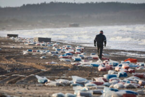 Mężczyzna spaceruje po obszarze, na którym utknęło kilka kontenerów, zgubionych na Morzu Północnym podczas sztormu Pia, Dania, 23.12.2023 r. (CLAUS BJOERN LARSEN/PAP/EPA)